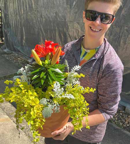 staff member smiling multiple plants arranged in a planter with red flowers.