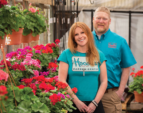 smiling store owners in front of vibrant flowers.